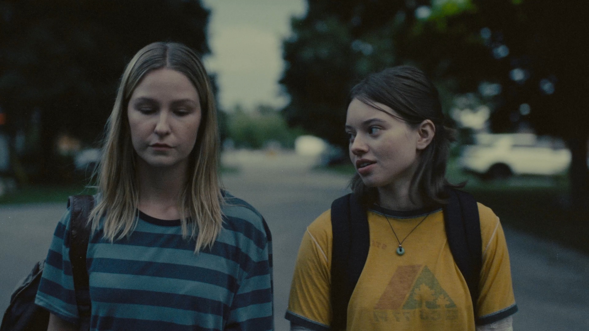 two teenage looking people with their backpacks on, walking down a street having a conversation